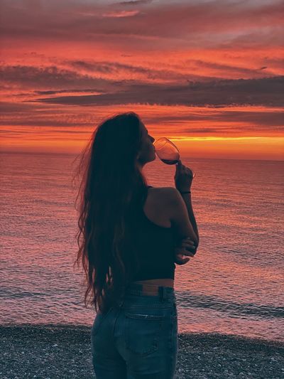 Woman standing by sea against orange sky