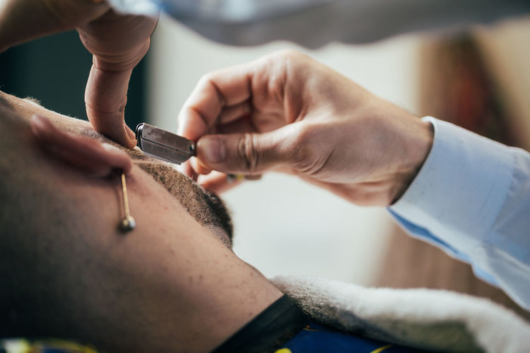 A barber cuts the beard of a man with a razor in a barbershop