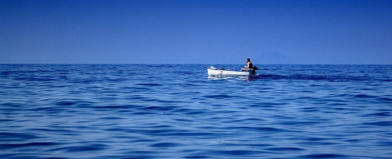 Man sitting in boat on sea against blue sky