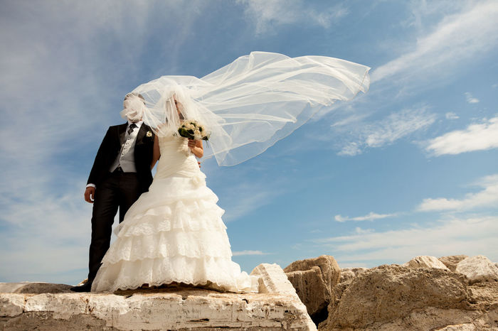 Low angle view of bride and groom standing on rocks against sky