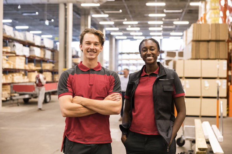 Portrait of smiling salesman with arms crossed standing with female staff at hardware store