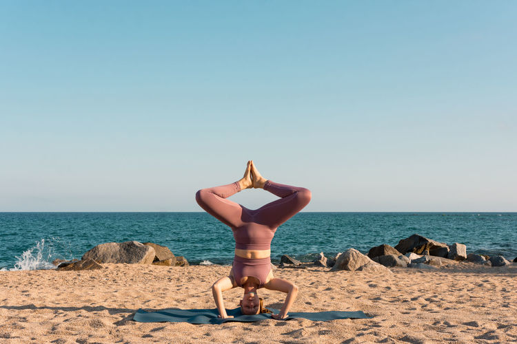 Relaxed female balancing in salamba sirsasana on mat while doing yoga on seashore