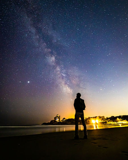 Silhouette of man star gazing on the beach under the milkyway galaxy.