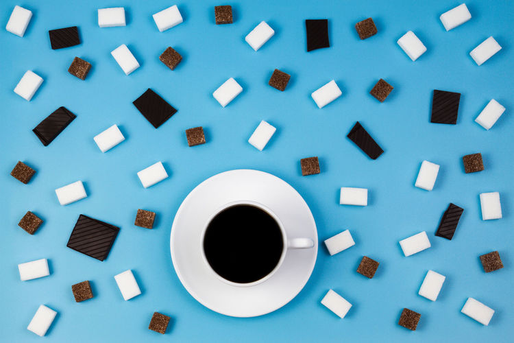 Directly above shot of black coffee with sugar cubes on blue background