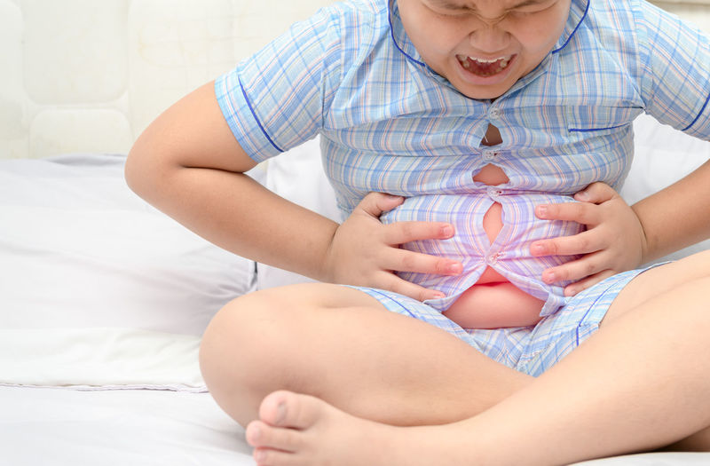 Digital composite image of boy holding abdomen in pain while sitting on bed