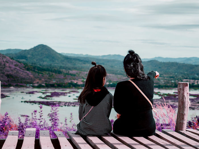 Rear view of mother and daughter looking at landscape while sitting on boardwalk