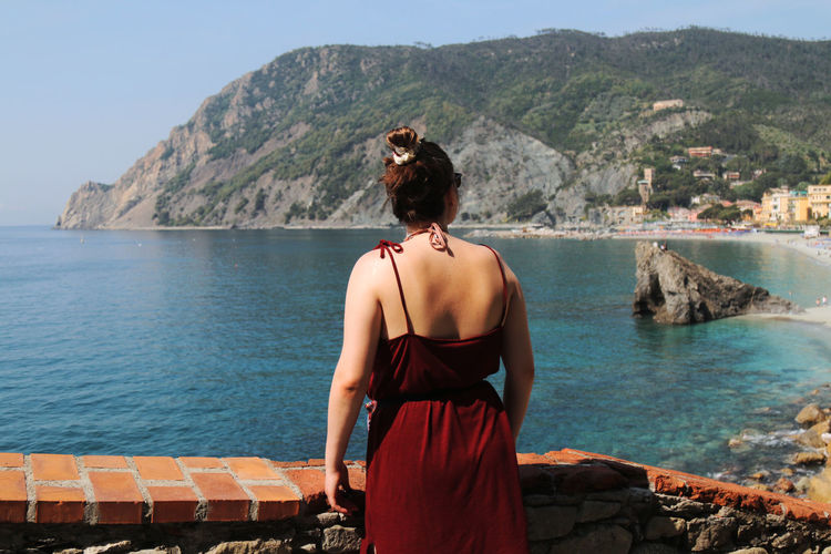 Rear view of woman wearing red dress while standing by retaining wall against sea