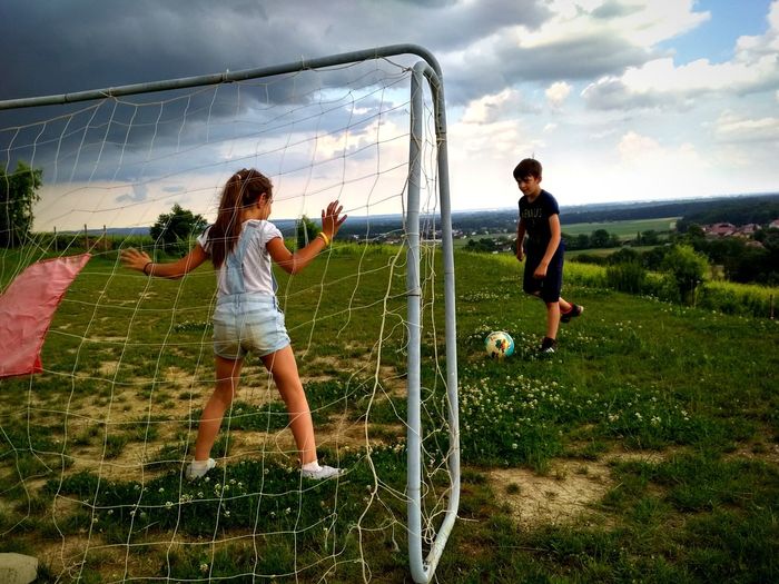 Friends playing soccer on field against sky