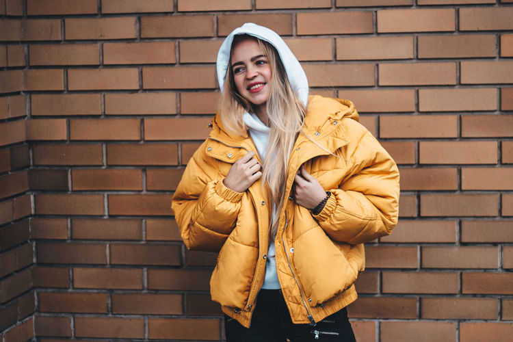 Young woman wearing yellow jacket standing against brick wall