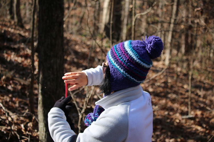 Rear view of woman wearing knit hat using phone at forest