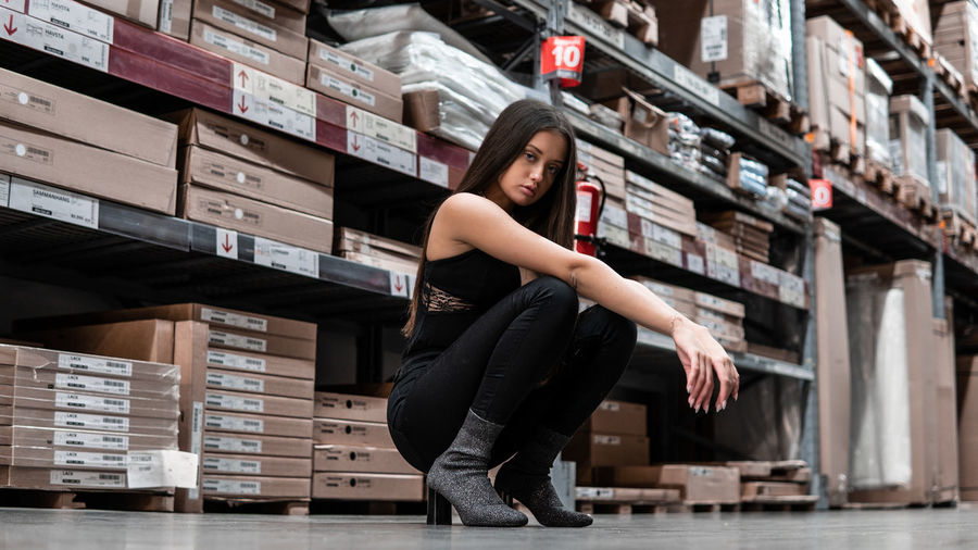 Full length portrait of young woman crouching on floor in warehouse