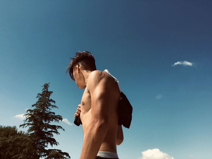 Low angle view of shirtless man standing against blue sky