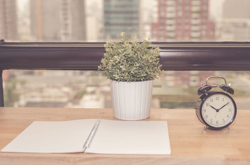 Close-up of book with potted plant and alarm clock at desk in office