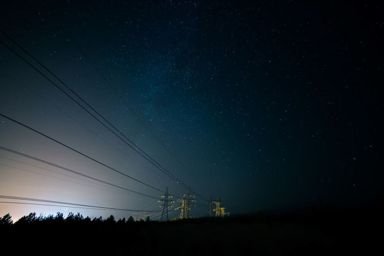 Silhouette electricity pylons against sky at night