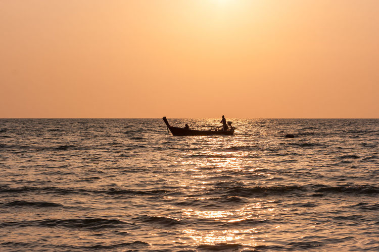 Silhouette people on boat in sea against clear orange sky