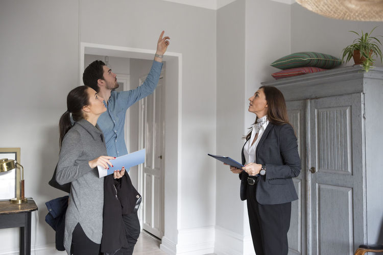 Woman and female realtor looking at man pointing up while standing in room