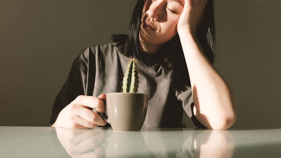 Diet concept. young upset woman holds in her hands a coffee cup with a cactus
