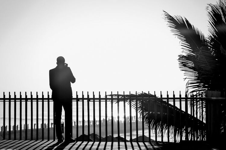 Silhouette man standing by railing against clear sky