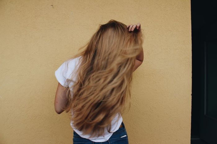 Rear view of woman with tousled hair standing against wall