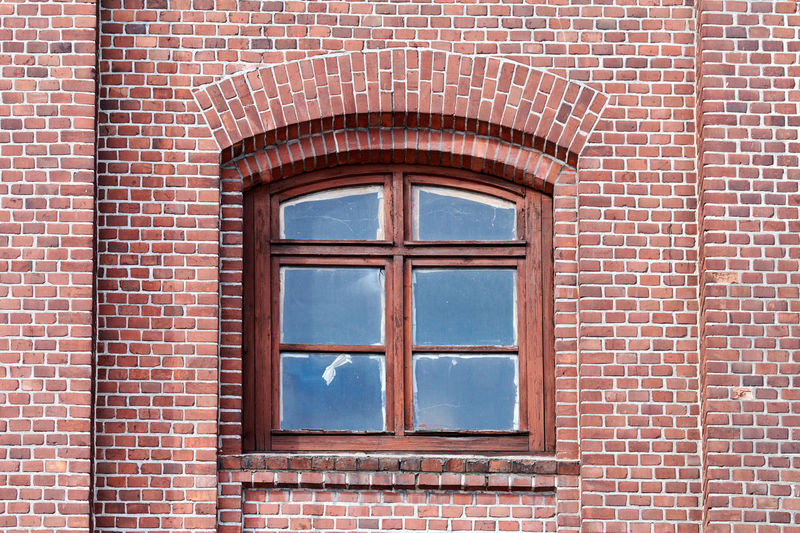 One arched glass window on old red brick wall. vintage window in brown wooden frame, red brick wall