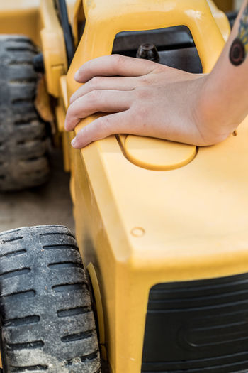 Child hand close up playing with yellow tractor in sand