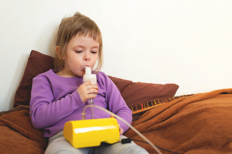 Sick child lies in bed and makes inhalation using a nebulizer.. treatment of cough with inhalation