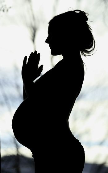 Silhouette pregnant woman practicing yoga against sky