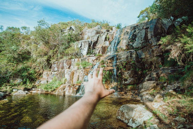 Cropped hand gesturing towards waterfall