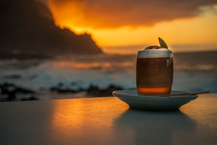 Close-up of drink on table against sea during sunset