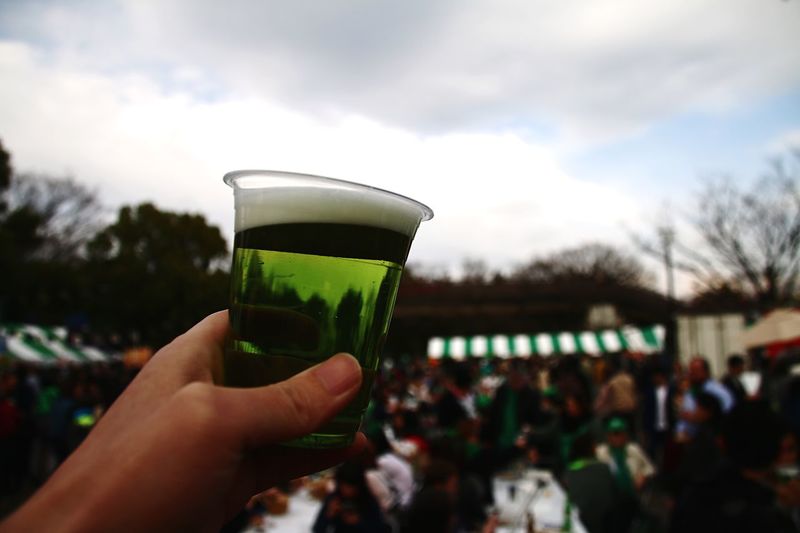 Cropped image of person holding beer glass against sky during st patrick day