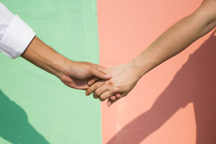 Cropped image of people with holding hands against wall