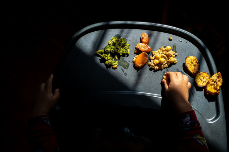 High angle view of a toddler's hands exploring a tray of brightly colored foods during mealtime