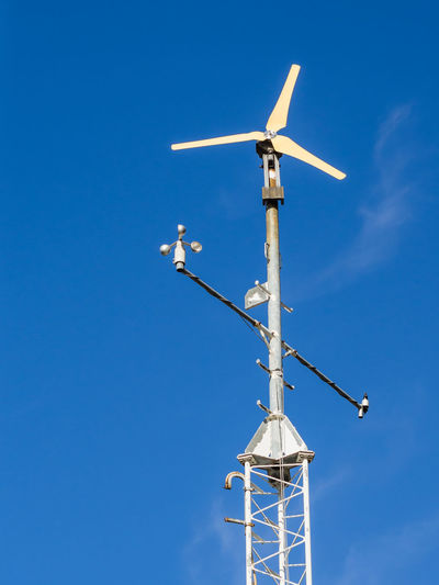 Low angle view of anemometer tower against blue sky