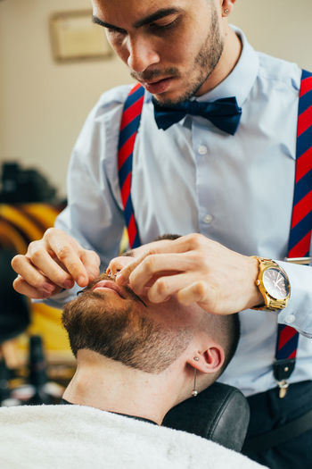 A barber cuts the beard of a man with a razor in a barbershop