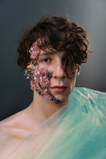 Portrait of young man with plant parts on face against gray background