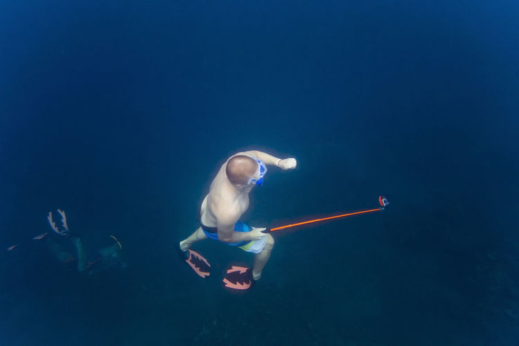 High angle view of man holding monopod while swimming with friends undersea