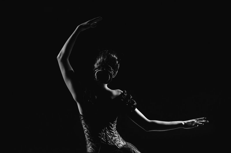 Midsection of dancer with raised arms against black background