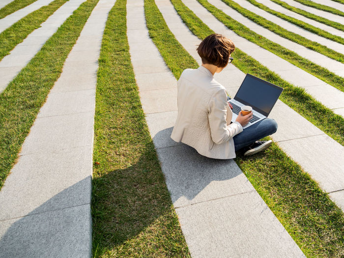 Business woman is working remotely in park with laptop. casual clothes. freelance job outdoors.