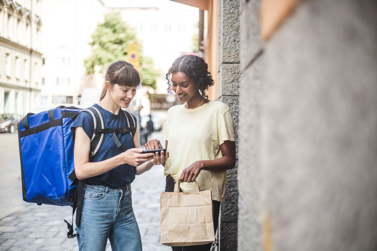 Delivery woman taking sign from female customer while delivering package