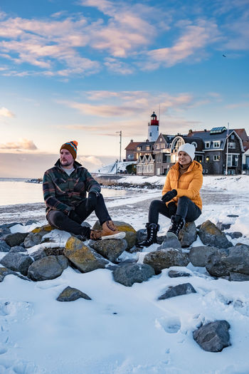 Couple sitting on rock against sky during winter