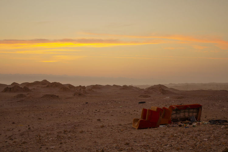 Vintage sofa throwed into garbage in the middle of the desert during golden sunset