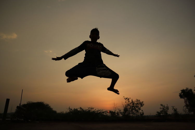 Side view of woman jumping against sky during sunset