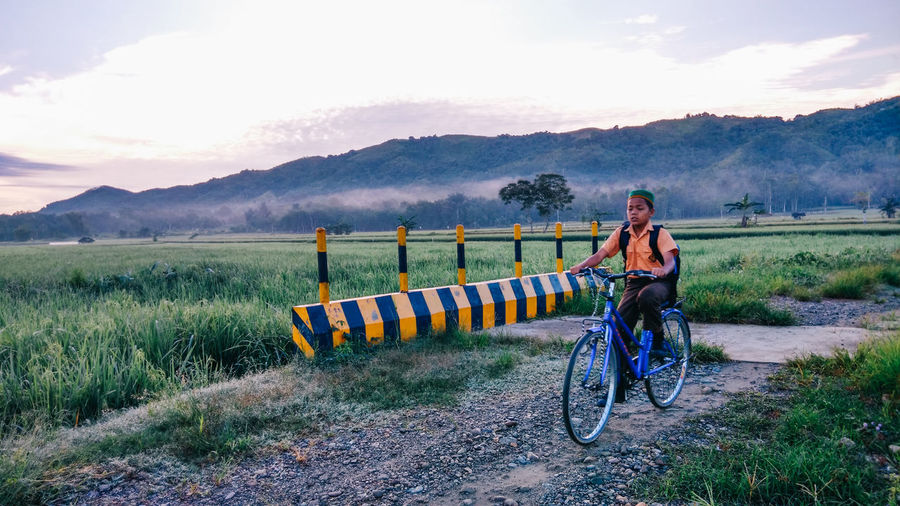 Teenage boy riding bicycle on dirt road amidst field