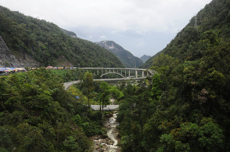 Arch bridge amidst trees and mountains against sky