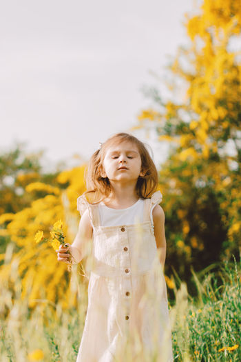 Portrait of young woman standing against yellow flower