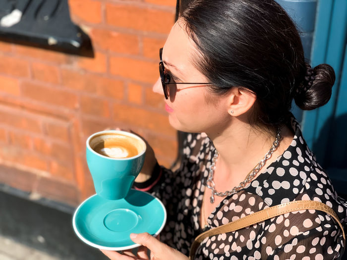 Young candid woman drinking morning coffee in tiffany color ceramic mug with saucer on cafe terrace.