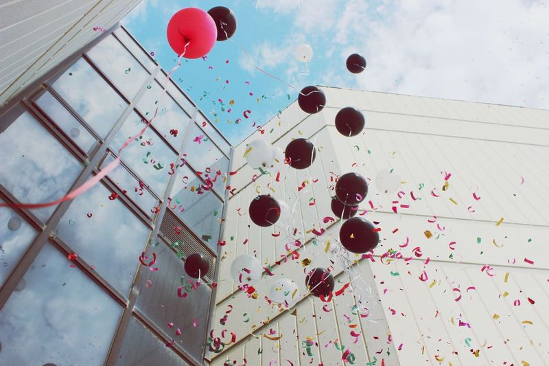 Low angle view of balloons and confetti in mid-air by building