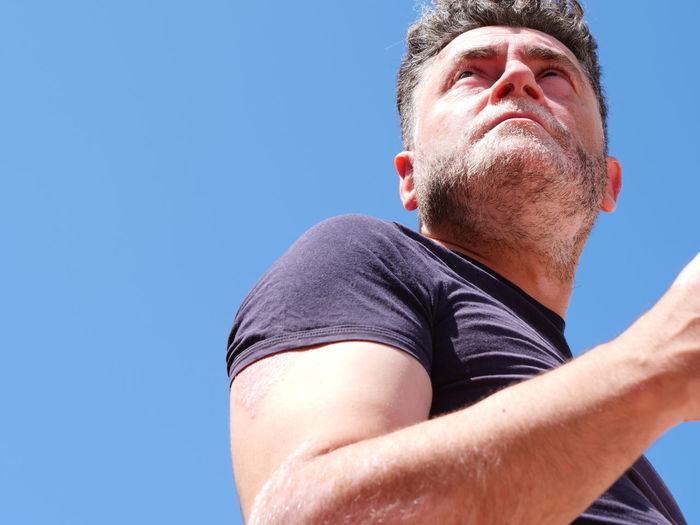 Low angle view of man looking away against clear blue sky