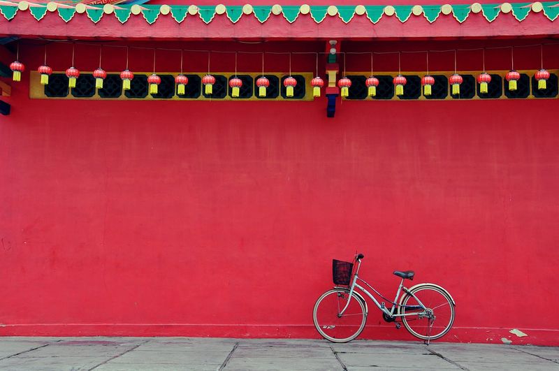Bicycle parked on street against red wall