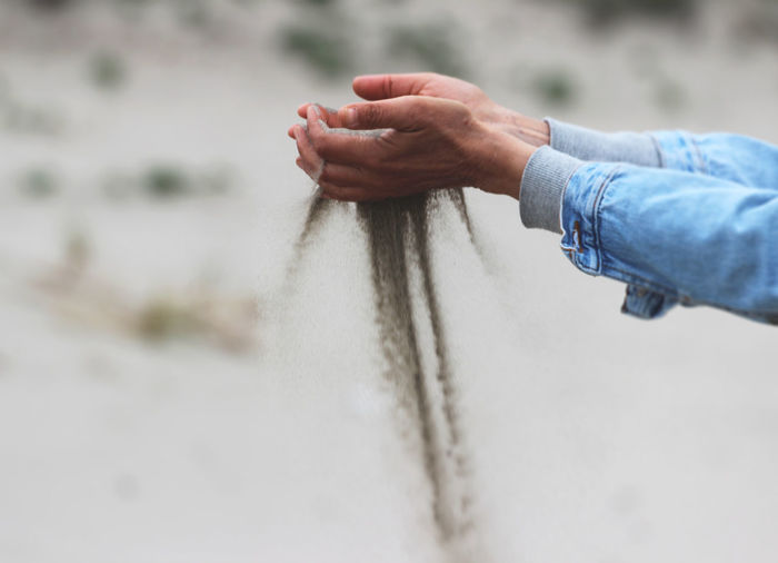 Cropped hands of man holding sand at desert